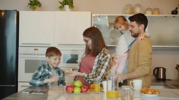 Люблячі батьки батько і вагітна мати обіймають дітей, висловлюючи любов під час сніданку — стокове відео
