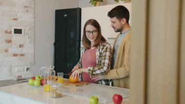 Hamile kız mutfakta yemek pişiriyor ve kocasını bebekle kucaklarken besliyor.