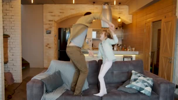 Movimento lento de jovem pai alegre e linda filhinha dançando pulando no sofá rindo se divertindo — Vídeo de Stock