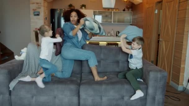 Misturado raça senhora babá jogando travesseiro luta com crianças rindo se divertindo dentro de casa — Vídeo de Stock