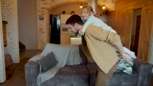 Verspielter junger Mann hat Spaß mit süßer kleiner Tochter, die Kind trägt und im Haus tanzt — Stockvideo