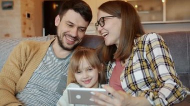 Mutlu insanlar anne, baba ve kız akıllı telefon kullanarak ekrana bakıp evde gülüyorlar.