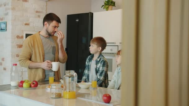 Любимый отец разговаривает с семьей беременной женой и обожаемыми детьми на кухне дома — стоковое видео