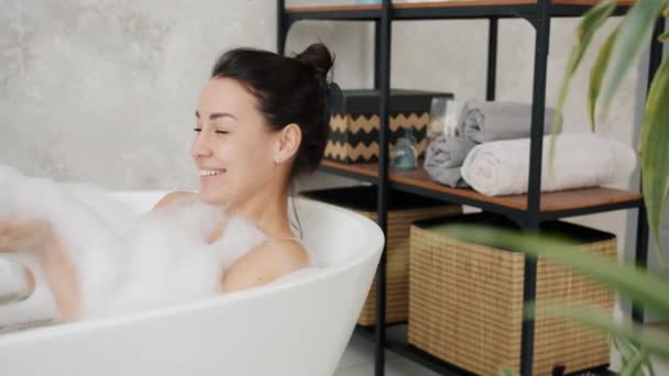 Movimento lento de estudante do sexo feminino desfrutando de banho quente com espuma sorrindo relaxante em casa — Vídeo de Stock