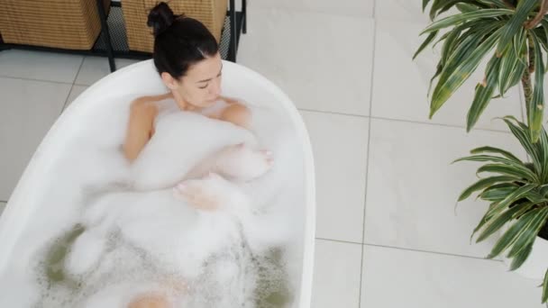 Високий кут зору привабливої леді лежить у ванні, розслабляючись у теплій воді з бульбашками — стокове відео