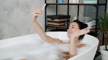 Online video görüşmesi sırasında banyoda el sallayan neşeli genç bayan.