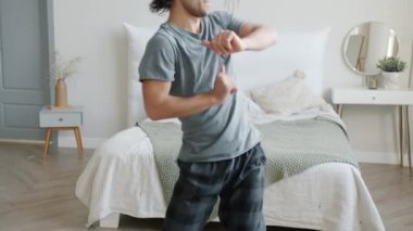 Yavaş hareket eden pijamalı adam dans ediyor yatak odasında kulaklıkla müzik dinliyor.