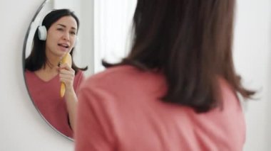 Kablosuz kulaklık takan komik kız banyoda saç fırçasında şarkı söylüyor, eğleniyor.