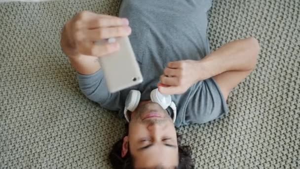 一个快乐的年轻人摆着姿势躺在床上拿着智能手机相机的倒影 — 图库视频影像
