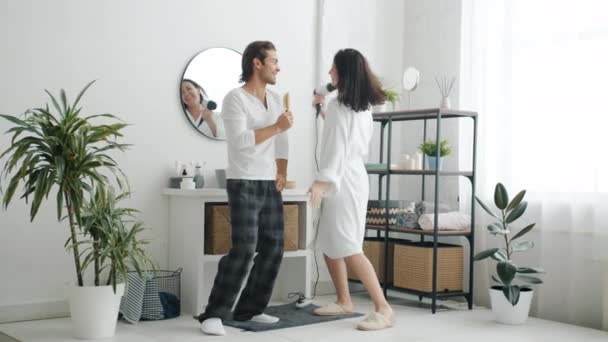Killen i pyjamas och tjejen i badrock dansar sjungande ha kul i badrummet — Stockvideo