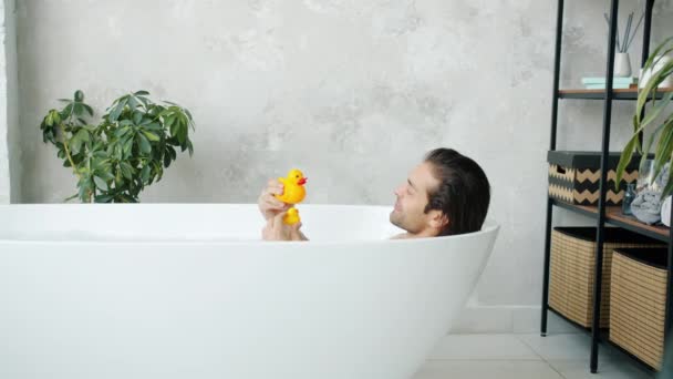 Oyuncak ördeklerle oynayan komik genç adam evde banyo yapıyor. — Stok video