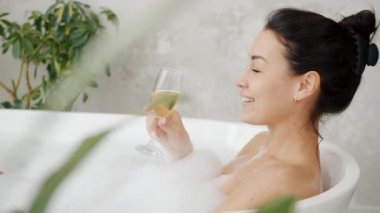 Sıcak bir banyoda şampanyanın keyfini çıkaran mutlu kızın yavaş yavaş gülümsemesi evde dinleniyor.