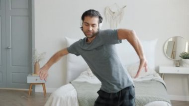 Yatak odasında pijama giyen, kulaklık takan hoş görünümlü bir adamın yavaş çekimleri.