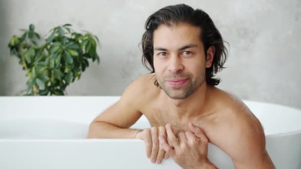 迷人的年轻人面带微笑地看着独自躺在浴缸里的相机的画像 — 图库视频影像