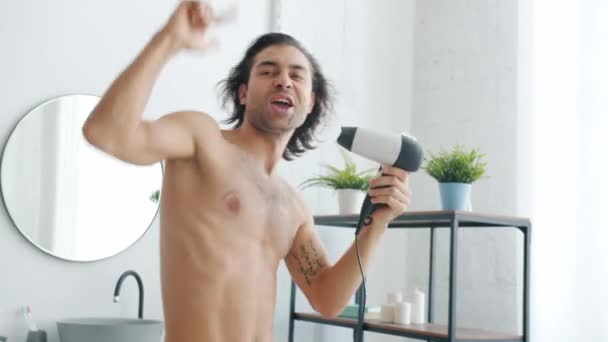 Brunet créatif s'amusant à la maison dansant et chantant dans le sèche-cheveux dans la salle de bain — Video