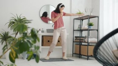 Pijamalı, dans eden, şarkı söyleyen, banyoda kulaklık takan güzel bir kadının yavaş çekimleri.