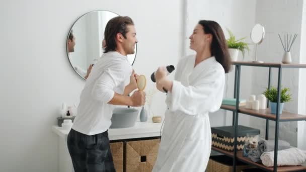 Mooi koppel dansen en zingen met haarborstel en föhn in de badkamer — Stockvideo