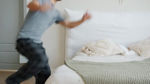 Szczęśliwy facet w piżamie biegnie do łóżka skacząc relaksując się korzystając z wypoczynku w domu — Wideo stockowe