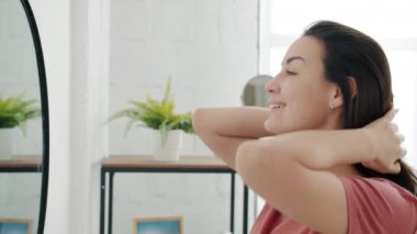 Saçlarını elleriyle tarayan ve banyodaki aynaya bakan çekici bir genç kız portresi.