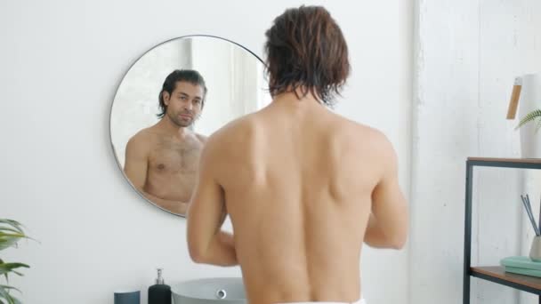 Медленное движение красивого парня, смотрящего на мускулы в зеркале, наслаждающегося красотой тела в ванной — стоковое видео