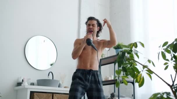 Портрет радостного парня, поющего в фен, танцующего весело в ванной — стоковое видео