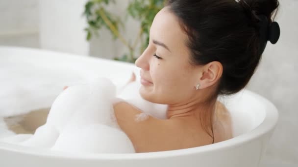 Крупним планом красива дама миє у ванній з піною посміхаючись насолоджуючись теплою водою — стокове відео