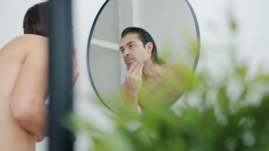 Yakışıklı genç adam aynaya bakıyor. Yüzüne dokunuyor. Sonra baş parmağını kaldırıyor ve gülümsüyor.