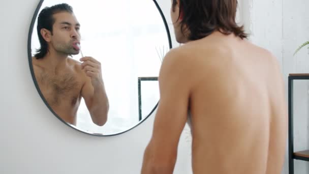 Zpomalený pohyb mladého muže čistí zuby a pak se dívá do zrcadla v koupelně — Stock video