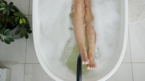 Close-up de pernas femininas em movimento na banheira desfrutando de água morna e bolhas de espuma — Vídeo de Stock