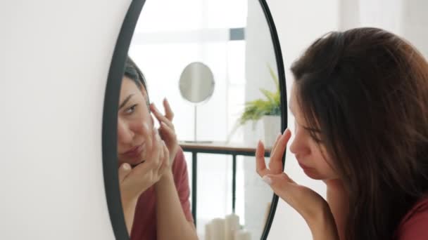 Медленное движение молодой женщины касаясь лица ищет недостатки на коже в ванной комнате — стоковое видео