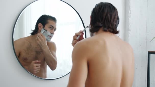 Portret młodego bruneta golenie brody z brzytwą rano w łazience — Wideo stockowe