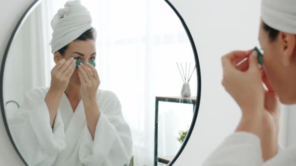 Красива молода жінка наносить плями очей, дивлячись на дзеркало у ванній кімнаті і посміхаючись — стокове відео