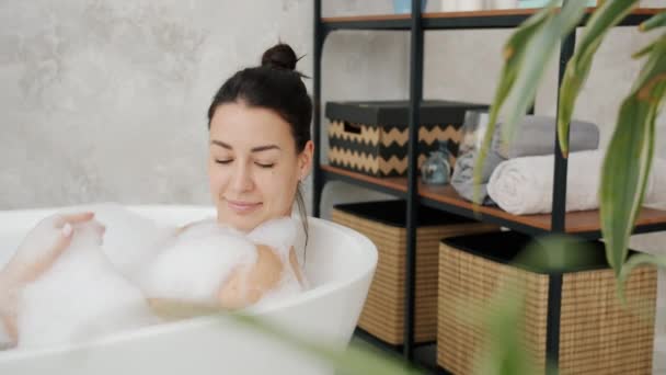 Bella signora lavaggio in vasca pulizia della pelle con schiuma sorridente godendo il relax a casa — Video Stock