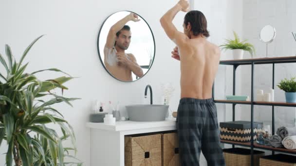 Visszapillantás a fiatal férfi pizsama nadrág borotválkozás hónalj borotvával a fürdőszobában — Stock videók
