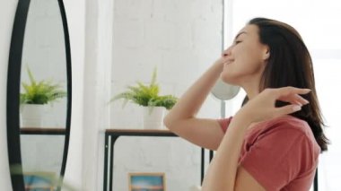 Modern banyoda aynaya bakarak saç stili seçen güzel bir kadının yan görüntüsü.