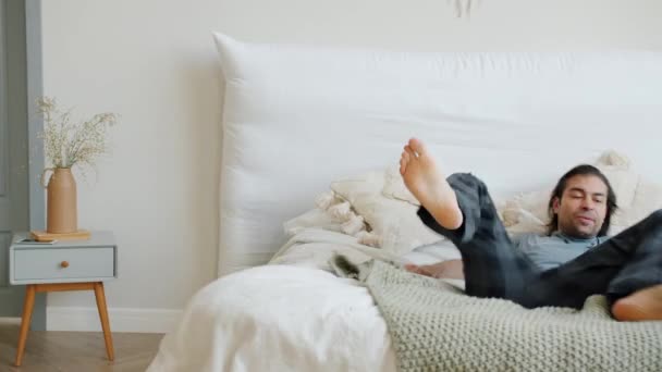 Cámara lenta de joven feliz corriendo a la cama y luego relajarse disfrutando del descanso en casa — Vídeos de Stock