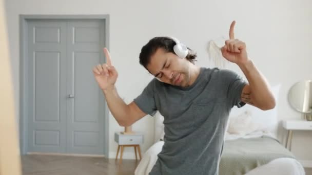 Speelse man heeft plezier thuis dansen en gebaren poseren voor de spiegel het dragen van een koptelefoon — Stockvideo