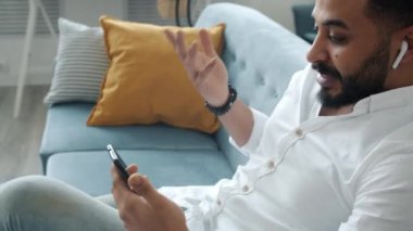 Çevrimiçi video görüşmesinde konuşan neşeli melez adam evdeki akıllı telefon ve hava araçlarını kullanıyor.