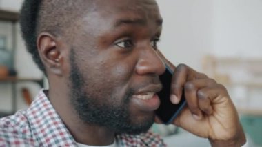 Cep telefonuyla gülen Afro-Amerikalı bir adamın yakın plan portresi.