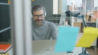 Laptopla çalışan ve ofiste müzik dinleyen olgun, kır saçlı bir adam.