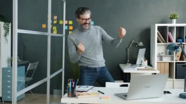 Neşeli olgun iş adamı dans ediyor, ofiste rahatlarken eğleniyor.