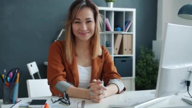 Ofisteki kameraya bakıp gülümseyen genç bir iş kadınının portresi.