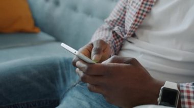 Mutlu Afrikalı Amerikalı adam evde akıllı telefon kullanıyor. Kanepede yalnız başına dinleniyor.
