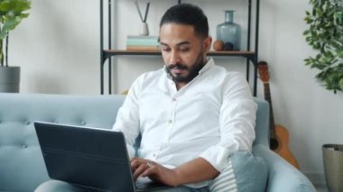 Orta Doğulu çekici bir adamın evde dizüstü bilgisayar kullanması ve serbest yazı yazması.
