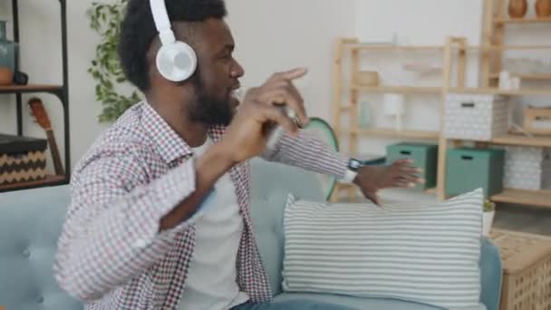 Joyeux jeune homme avec écouteurs et smartphone profitant de la musique et la danse à la maison — Video