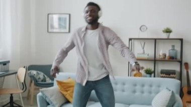 Modern apartmanda kablosuz kulaklık takıp dans eden Afro-Amerikalı adam.