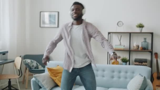 Afro-Américain gars danse avoir du plaisir à porter des écouteurs sans fil dans un appartement moderne — Video