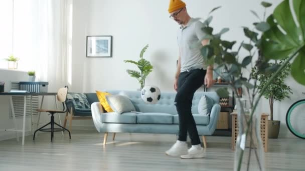 Deportivo joven pateando pelota jugando al fútbol en el interior en el apartamento solo — Vídeos de Stock