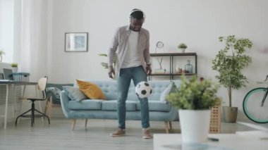 Kablosuz kulaklık takan Afrikalı adam apartmanda top oynarken eğleniyor.