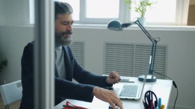 Olgun iş adamı gözlük takıyor. İşte bilgisayar kullanıyor. Masada yazı yazıyor.
